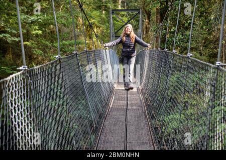 Donna che attraversa un ponte sospeso su un ruscello sulla pista Kepler. Foto Stock