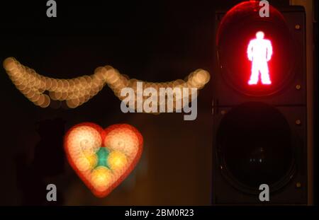 Foto notturna di un semaforo rosso per pedoni accanto a lampade decorative a forma di cuore Foto Stock
