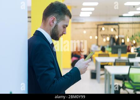 Ritratto di giovane uomo d'affari caucasico bearded vestito casual smart utilizzando il telefono all'interno di moderno spazio di coworking. Foto Stock