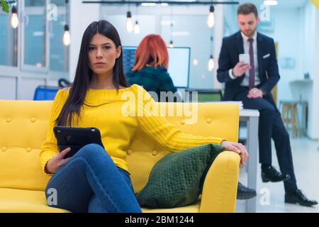 Ritratto di giovane bella ragazza casual felice in maglione seduta al suo posto di lavoro all'interno di moderno co-lavoro spazio. Foto Stock