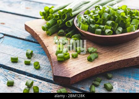 Cipolla fresca verde tritata e si trova su una ciotola su un tagliere su uno sfondo di tavole blu. Le cipolle sono ricche di vitamine e minerali. Foto Stock