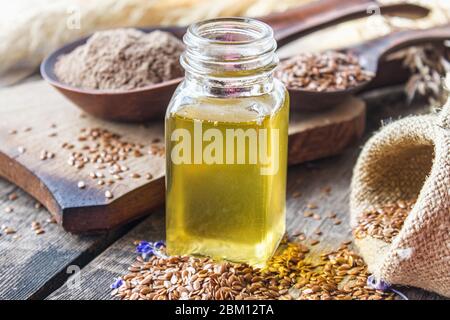 Olio di lino in un vaso vicino ai semi di lino su uno sfondo di vecchi assi. L'olio di semi di lino viene usato in cucina, medicina, cosmetologia. Foto Stock