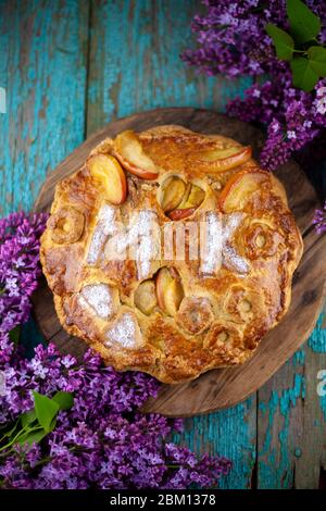 Torta rotonda fatta in casa con mele su un tavolo di legno. Un bouquet di lilac. Le lettere MK . Pasta semplice a base di pasta frolla e caramellata Foto Stock