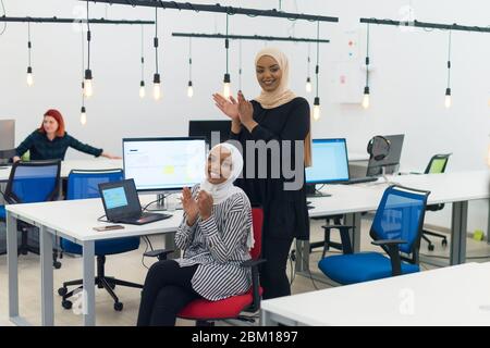 Due allegre e fiduciose donne musulmane africane hijab business applauding e sorridente, il successo e il concetto di successo Foto Stock