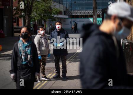 Gli acquirenti che indossano maschere facciali protettive si trovano a 2 m di distanza in coda per una banca di strada alta a East Ham, Londra est, mentre il Regno Unito continua a chiudere a chiave per contribuire a frenare la diffusione del coronavirus. Foto Stock