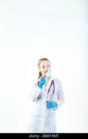 l'infermiere del medico mette su una maschera protettiva. Un infermiere in una maschera respiratoria. Indossare le maschere. Indossare guanti. Bello medico biondo mostra come indossare un protec Foto Stock