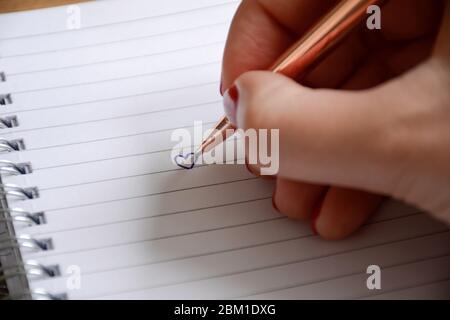 La mano femminile curata disegna un cuore nel notebook. San Valentino e concetto di amore. Foto Stock