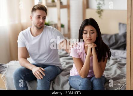 Marito che tocca offeso moglie spalla seduto a letto a casa Foto Stock