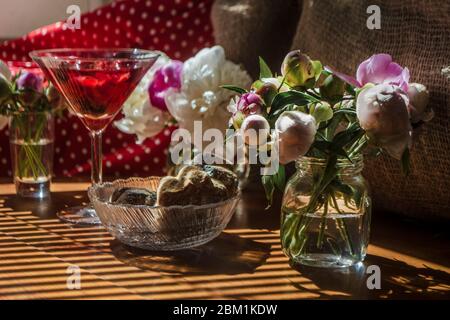 Solenne vita rustica con bicchiere di bevanda rossa con torte in una ciotola circondata da fiori bianchi su sfondo tessile su tavolo di legno. Stri diagonali Foto Stock