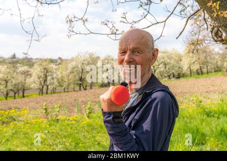 Girovita foto di un felice anziano pensionato in abbigliamento sportivo che tiene il manubro rosso e guardando la macchina fotografica Foto Stock