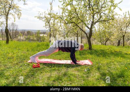 Vecchio uomo anziano che fa asse sul tappeto di yoga nel parco Foto Stock