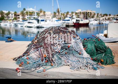 Pile di pescatori´s reti da pesca su un molo in un porto. Barche e case mediterranee sullo sfondo. Foto Stock