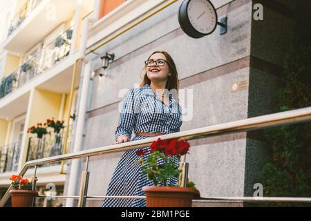 Il tema dell'affitto di una casa in Europa per le vacanze estive. Una giovane donna caucasica in un vestito posa su una terrazza di appartamenti decorati con Foto Stock