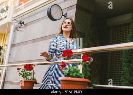 Il tema dell'affitto di una casa in Europa per le vacanze estive. Una giovane donna caucasica in un vestito posa su una terrazza di appartamenti decorati con Foto Stock