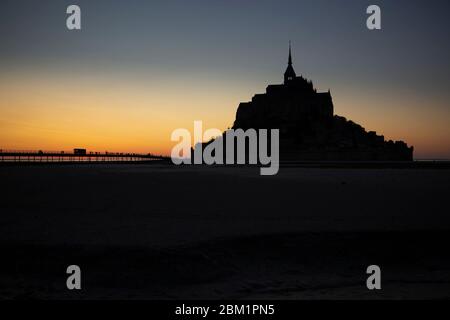 Tramonto silhouette di le Mont Saint Michel, Francia. La gente sta camminando sul ponte per visitare il monastero. Foto Stock