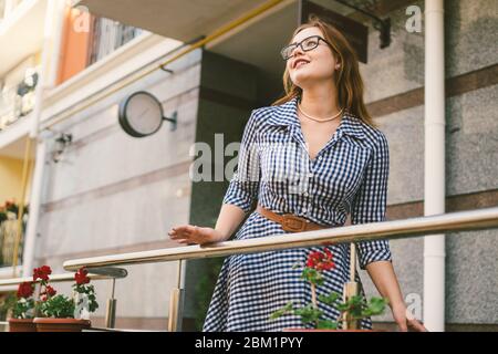 Il tema dell'affitto di una casa in Europa per le vacanze estive. Una giovane donna caucasica in un vestito posa su una terrazza di appartamenti decorati con Foto Stock