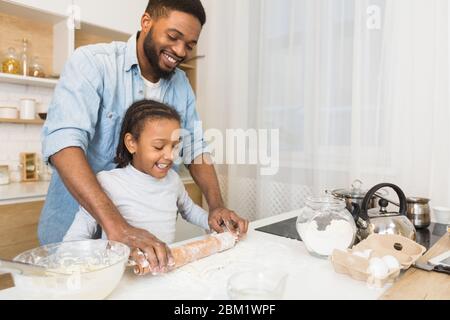 Sorrido padre africano e figlia che arrotola pasta insieme Foto Stock