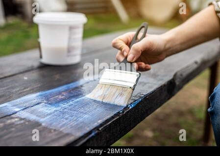 Un falegname di legno applica uno strato protettivo di vernice trasparente. Mano con un pennello da vicino sul piano del tavolo Foto Stock