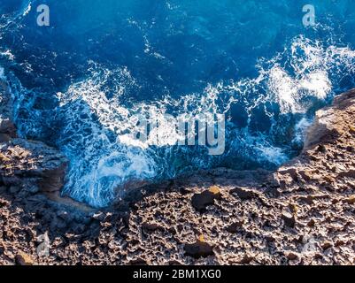 Vista dall'alto mare azzurro con onde che battono sulla spiaggia e sulle rocce. Foto aerea. Foto Stock