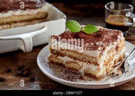 Primo piano su una porzione di dessert italiano tiramisù gourmet con un rametto di menta servito su un piatto al tavolo in una vista laterale Foto Stock