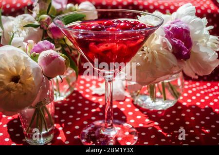 Magia solenne vita morta con bicchiere di bevanda rossa con bacche biologiche autunnali circondate da fiori bianchi nell'ombra diagonale a righe dei ciechi o Foto Stock