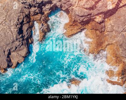 Vista dall'alto mare azzurro con onde che battono sulla spiaggia e sulle rocce. Foto aerea. Foto Stock