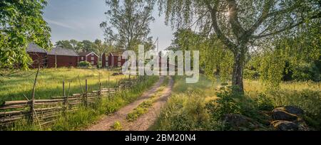 Piccola strada di campagna e vecchi cottage tradizionali rossi in un paesaggio rurale presso il villaggio Stensjo by. Oskarshamn, Smaland, Svezia, Scandinavia Foto Stock