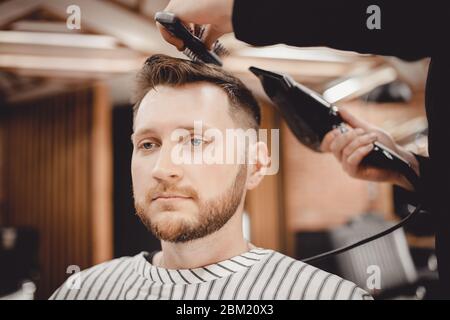 Il primo piano master Barber fa acconciature e styling con asciugacapelli per i ragazzi. Concept Barbershop Foto Stock