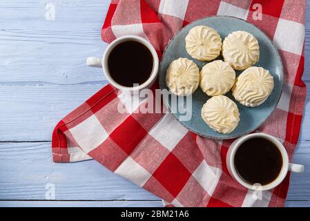Tazza di caffè americano e zephyr o marshmallow fatti in casa in un piatto blu su sfondo di legno blu chiaro. Foto Stock