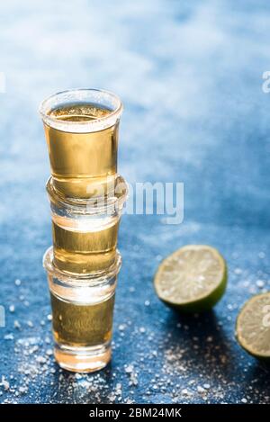 Tre colpi di tequila impilati, su un tavolo blu. Tequila in vetro d'oro con calce e sale. Alcol messicano forte e aromatico. Foto di festa. Foto Stock