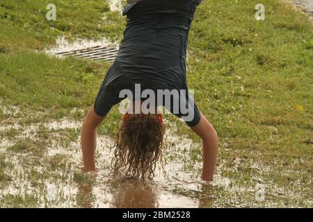 Giovane ragazza che si diverte bagnarsi in pozzanghere formatosi dopo una pioggia intensa Foto Stock