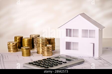 Casa con pile di monete con calcolatrice e piano di costruzione Foto Stock