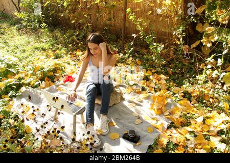 Adolescente che lavora su un notebook e che scatta foto all'esterno nel cortile in una bella giornata di autunno. Foto Stock