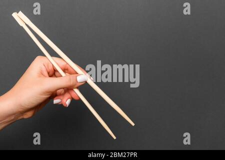 Immagine creativa delle bacchette di legno nelle femmine di mano su sfondo nero. Il giapponese e il cinese del cibo con copia spazio. Foto Stock