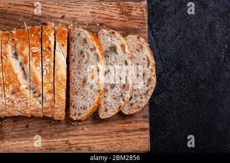 Primo piano pane integrale multigrain a fette fatte in casa con semi di lino e sesamo su tavola di legno su tavolo scuro. Foto Stock