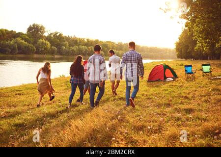 Gli amici si divertono a correre lungo il lago in un pic-nic in estate in autunno. Foto Stock