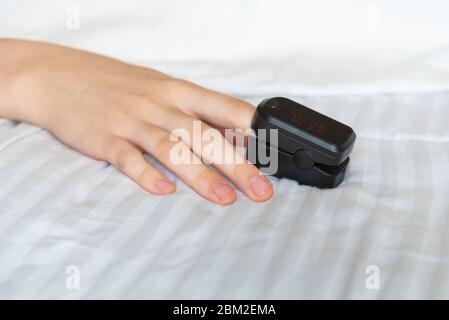 Primo piano della mano della donna che poggia sul letto, indossando un pulsossimetro per misurare la saturazione dell'ossigeno nel sangue Foto Stock