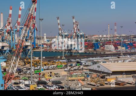 Gru di carico a quattro maglie sul molo con veicoli a motore parcheggiati pronti per la spedizione più gru di carico container in background, Ashdod Port, Israele Foto Stock