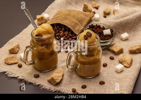 Caffè Dalgona in vasetto di muratori. Bevanda a base di caffè frusta coreana. Bevanda alla moda in quarantena, zucchero e chicchi di caffè su fondo in cemento di pietra nera Foto Stock