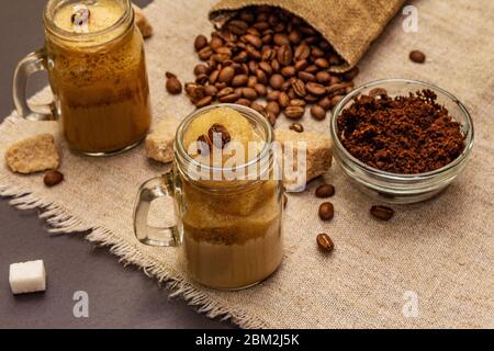 Caffè Dalgona in vasetto di muratori. Bevanda a base di caffè frusta coreana. Bevanda alla moda in quarantena, zucchero e chicchi di caffè su fondo in cemento di pietra nera Foto Stock