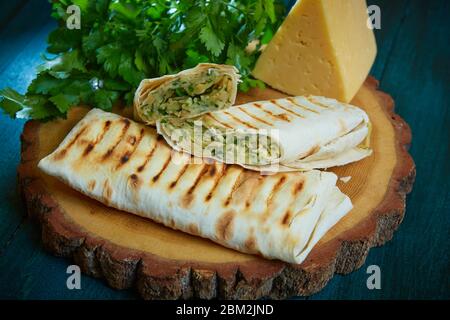 Shaurma arrotolare in una pita con formaggio ed erbe su sfondo ligneo Foto Stock