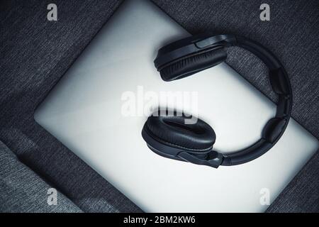 Computer portatile chiuso argento seduto sul divano grigio con cuffie wireless Big Black sulla parte superiore. Foto Stock