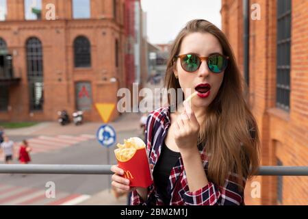 LODZ, POLONIA - 17 AGOSTO 2019: La ragazza mangia patatine fritte da una catena di ristoranti McDonald's. La ragazza sta avendo divertimento posando con il suo alimento. Foto Stock