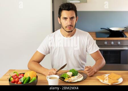 Un giovane fa colazione a casa in cucina. Il ragazzo mangia pane tostato e uova strapazzate con pancetta. Foto Stock