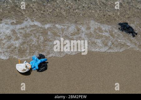 Maschere antivirus protettive e guanti di plastica spazzatura rifiuti sulla spiaggia sabbiosa, malattia da inquinamento da cocvidi coronavirus Foto Stock