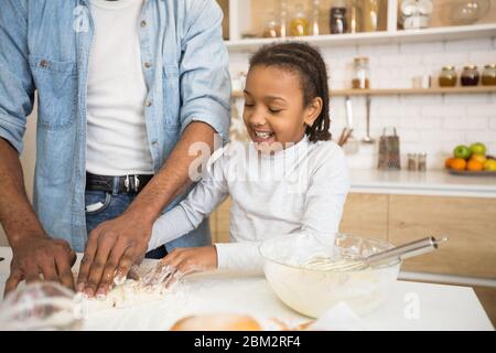 Figlia gioiosa che aiuta papà a impastare l'impasto Foto Stock