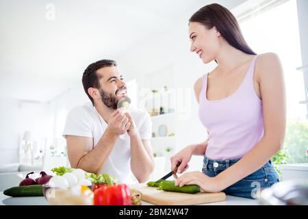 Ritratto di due persone hanno soggiorno a casa quarantena preparare fresco piatto vegetariano donna tagliato tagliando bordo cetriolo uomo guardare mangiare fetta in casa al chiuso Foto Stock