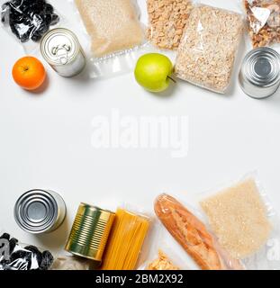 Vari alimenti sigillati in sacchetti di plastica, lattine e frutta su sfondo bianco, vista dall'alto. Concetto di donazioni di cibo Foto Stock