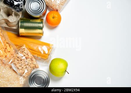 Vari alimenti sigillati in sacchetti di plastica, lattine e frutta su sfondo bianco, vista dall'alto. Concetto di donazioni di cibo Foto Stock