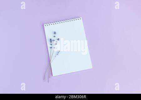 Notebook con pagina vuota e lavanda su sfondo viola. Disposizione piatta. Inserire il testo. Foto Stock